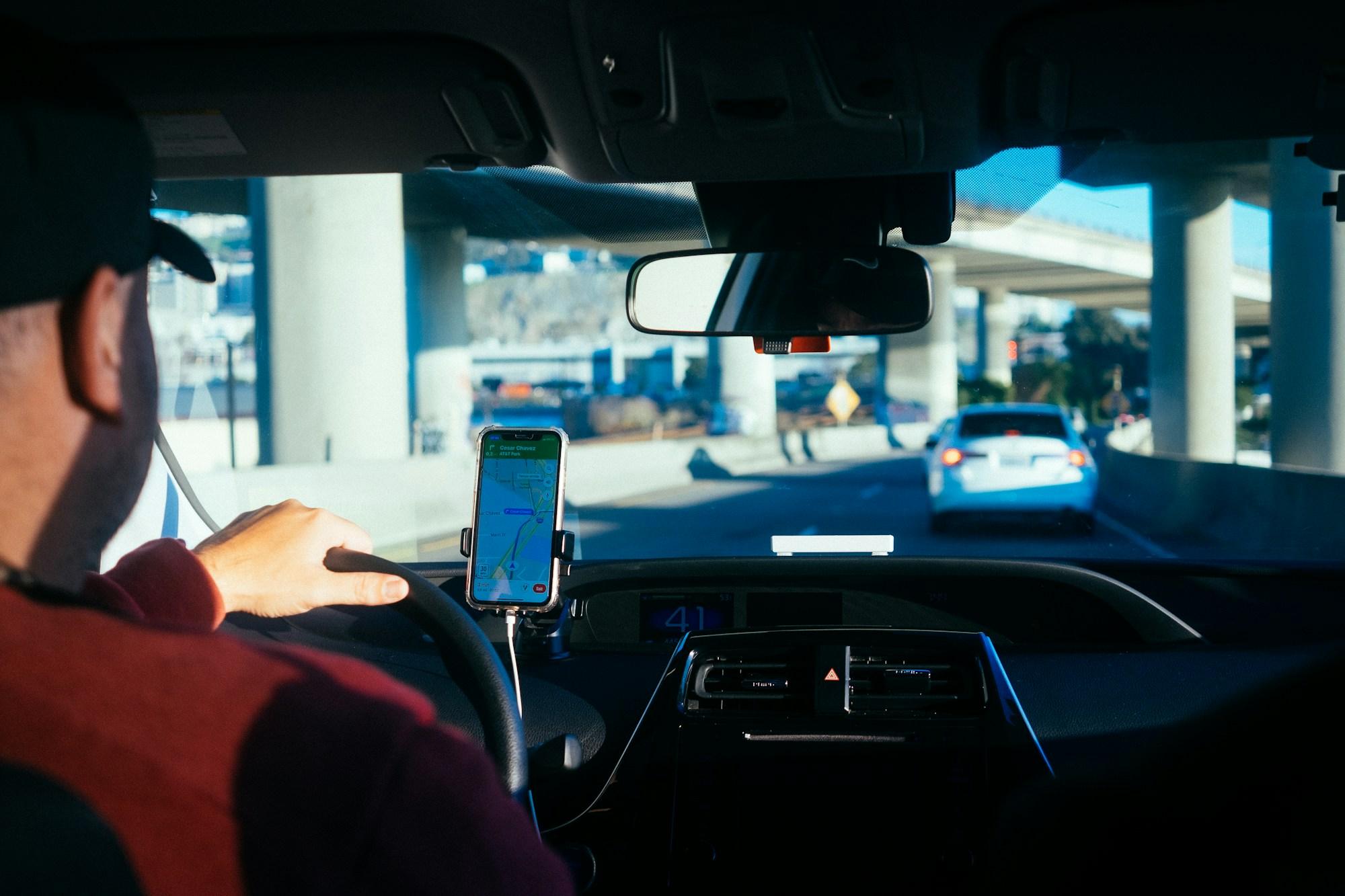 Driver behind the wheel with a phone navigation app mounted on the dash